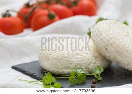 Closeup of round white homemade cheese - traditional milk creamy dairy product served with herbs and tomatoes on vintage black board. Rustic style.