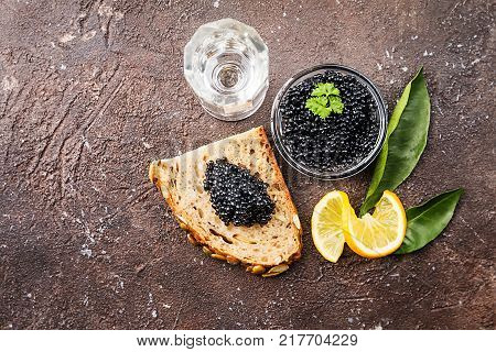 Black caviar in a glass bowl with lemon close up over dark background, top view