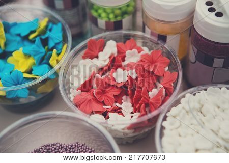 Ice cream treats and toppings sale. Rainbow sprinkles, stars, non pareil and glitter cupcake decorations, bright red and white. Closeup in plastic plates with spoons. Confectionery store