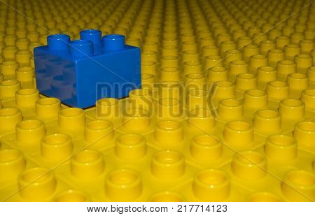 A sea of yellow building bricks all ligned up as far as they eye can see with one solitary blue block sitting on top.