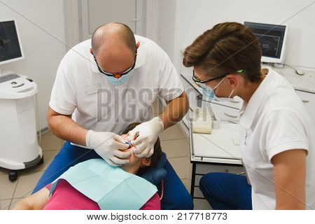 Process Of Preparing And Installing Dental Ceramic Crown. Male Professional Dentist And Female Assis
