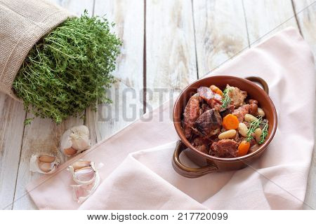 Cassoulet. Containing meat pork sausages goose duck and sometimes mutton and two types of white beans. French food (cuisine). On old wooden white background.