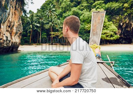 Tourist (young man) on the traditional long tail boat against lagoon. Koh Lao Lading Island (between Phuket and Krabi) in Thailand.