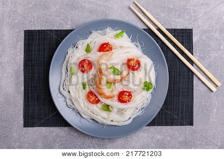 A top view on a chinese food. Chopsticks, shrimps and tomatoes on a rise nuddles on the marble background. Close-up of objects. Food concept.