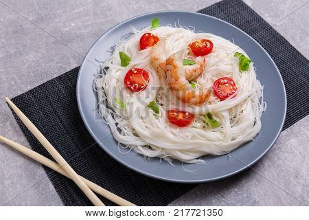 A top view on a chinese food. Chopsticks, shrimps and tomatoes on a rise nuddles on the marble background. Close-up of objects. Food concept.