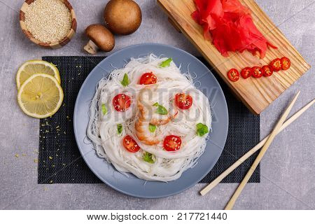 A top view on a chinese food. Chilli, chopsticks, shrimps mushrooms, slices of lemon and tomatoes on a rise nuddles on the marble background. Close-up of objects. Food concept.