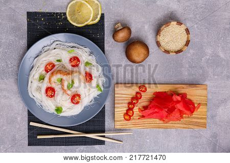 A top view on a chinese food. Chilli, chopsticks, shrimps mushrooms, slices of lemon and tomatoes on a rise nuddles on the marble background. Close-up of objects. Food concept.