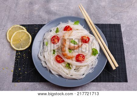 A top view on a chinese food. Chilli, chopsticks, shrimps and tomatoes and lemon on a rise nuddles on the marble background. Close-up of objects. Food concept.