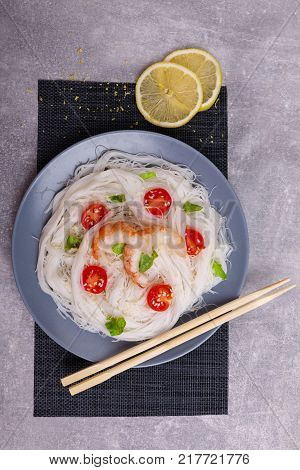 A top view on a chinese food. Chilli, chopsticks, shrimps and tomatoes and lemon on a rise nuddles on the marble background. Close-up of objects. Food concept.