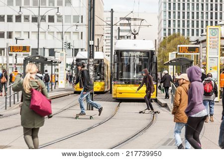 BERLIN GERMANY - APRIL 23 2016: Busy Alexanderplatz with yellow tram and people pedestrians and skaters crossing the street. Alexanderplatz is the main square in East Berlin.