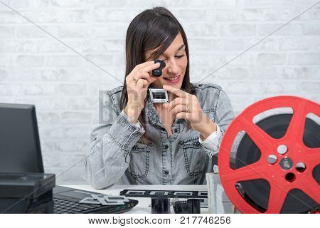 young brunette woman looking at film slide with a magnifying glass