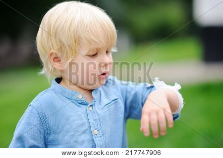 Cute little boy looking on his elbow with applied bandage. Child healthcare and medicine concept. First aid.