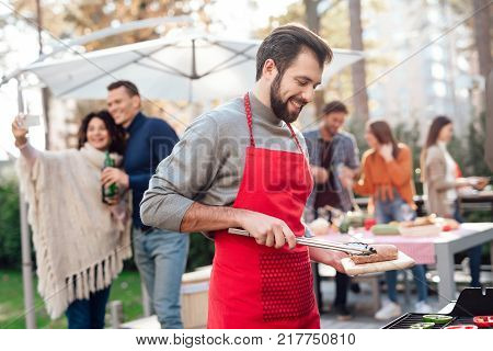 A man is cooking barbecue food. A company of young people came together for a barbecue. Friends have fun, they cook food, drink alcohol. They gathered in nature on a sunny day.