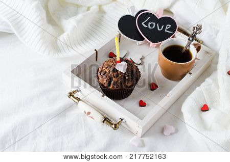 Muffins or capkakes with chocolate and black coffee on a wooden tray in bed. White background. Sweet food. Festive mood copy space flat lay