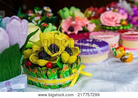 Close up hand-made present made of chocolate sweets put together with ribbon and aftificial yellow flowers