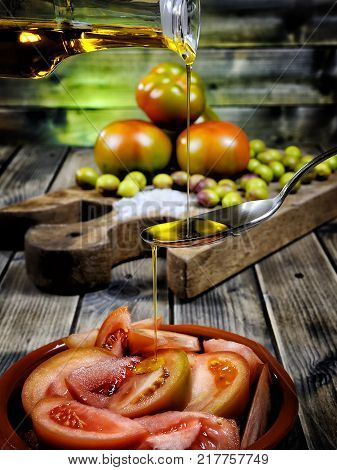 Close-up of an cruet pouring olive oil over tomato salad on an antique wooden table