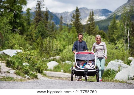 Senior couple and children in jogging stroller, summer day. High mountains in the background.