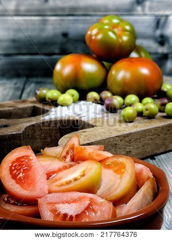 Close-up of an cruet pouring olive oil over tomato salad on an antique wooden table