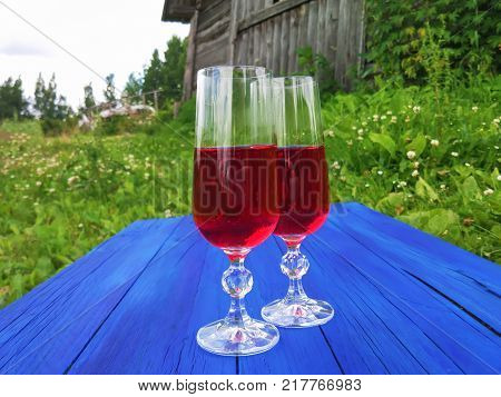 Two Glasses With Homemade Red Wine On Blue Boards Outdoors In Countryside At Summer.