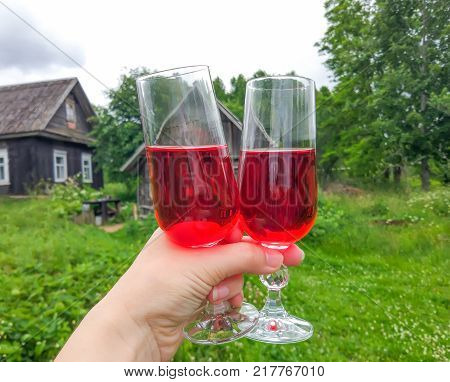 Two glasses with homemade red wine in a hand on farm yard background in countryside at summer.