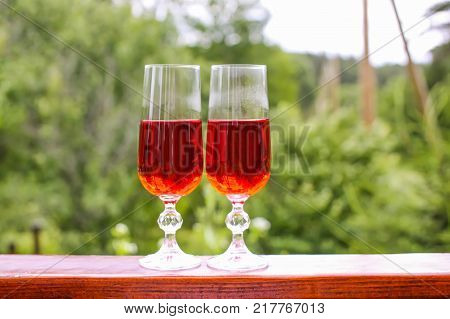 Two glasses with homemade red wine in summer park.