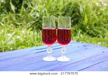 Two Glasses With Homemade Red Wine On Blue Boards Outdoors In Countryside At Summer.