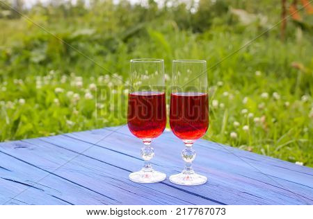 Two glasses with homemade red wine on blue boards outdoors in countryside at summer.
