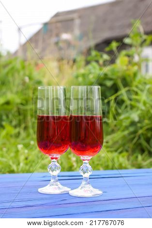 Two glasses with homemade red wine on blue boards outdoors in countryside at summer.