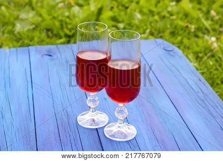 Two glasses with homemade red wine on blue boards outdoors in countryside at summer.