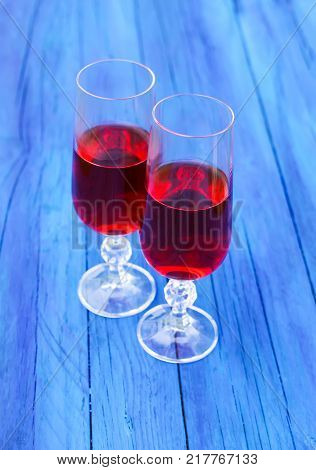 Two glasses with homemade red vine on blue boards outdoors in countryside at summer.