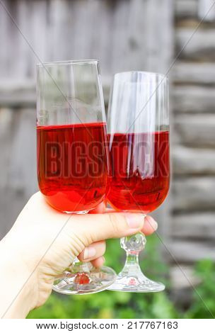 Two glasses with homemade red wine in a hand on farm yard background in countryside at summer.