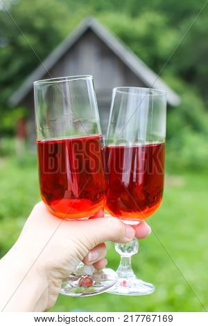 Two glasses with homemade red vine in a hand on farm yard background in countryside at summer.
