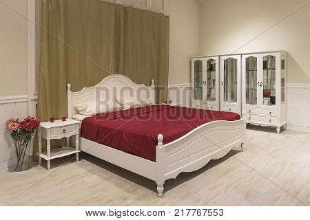 White wooden bed with dark red blanket and white pillows. The room Bridal Suite in an expensive hotel. A cozy bedroom. a chest of drawers, mezzanine, bedside table, coffee table