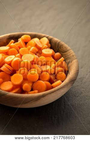 Carrot slices in wooden bowl. Fresh cut crisp slivers of Daucus carota, a root vegetable with orange color. Edible taproot pieces. Isolated macro food photo close up from above