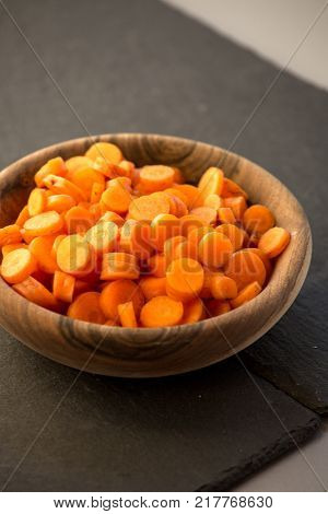 Carrot slices in wooden bowl. Fresh cut crisp slivers of Daucus carota, a root vegetable with orange color. Edible taproot pieces. Isolated macro food photo close up from above