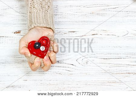 The hand that squeezed the red hearton wooden table. Love concept with copyspace.