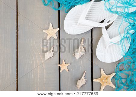 Seashells and white flip flops grey wooden background. Flat lay