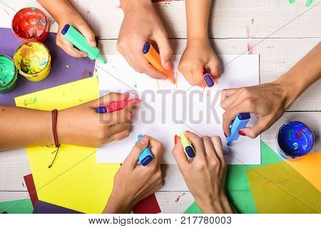 Artists wooden table with paints and colored paper. Art and artwork concept. Hands hold colorful markers and draw top view. Markers in male and female hands draw on blank white paper copy space