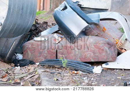 Mattress of bed or couch thrown in the garbage near metal disposal dumpster with front damaged car bumper on the street in the city