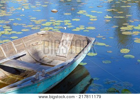 Old wooden rowboat painted in wethered green color tied up. Water lilys on the water