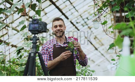 Young smiling blogger man florist in apron talking and recording video blog for his online vlog about the gardening