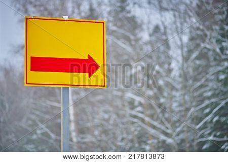 Yellow direction sign with red arrow on winter forest background