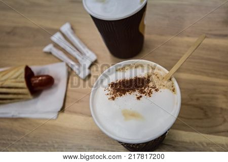 Hot dog and two cups of coffee on wooden table, focus on the foam of coffee