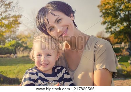 Happy joyful mother having fun throws up in the air child in autumn park.