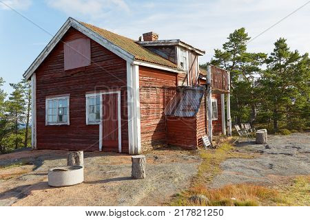 Red wooden abandoned cottage built on the rock pine trees in the background