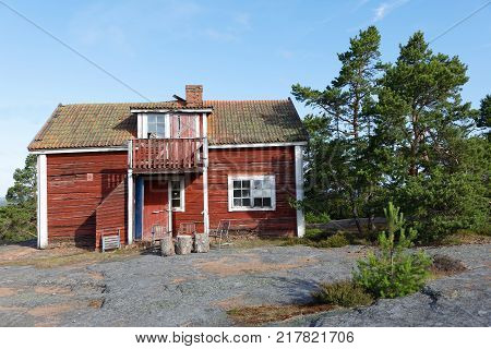 Red wooden abandoned cottage built on the rock pine trees in the background