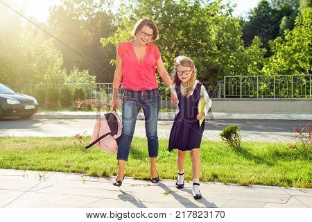 Mom and pupil of elementary school  holding hands. The parent takes the child to school. Outdoors, return to the concept of the school.