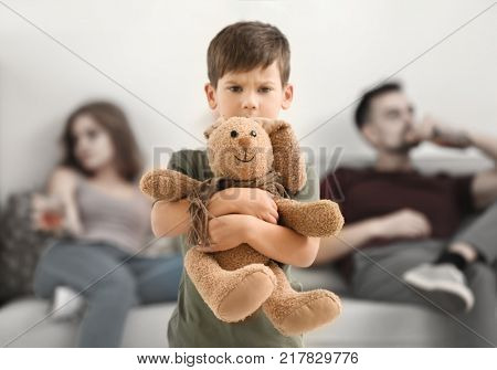 Upset little boy hugging toy bunny while his parents drinking alcohol on background