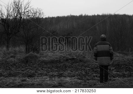 A woman stands turned back and looks at the dark forest