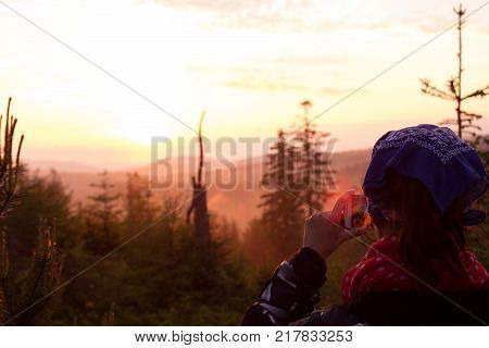 A young girl takes pictures of a mountain landscape at sunset